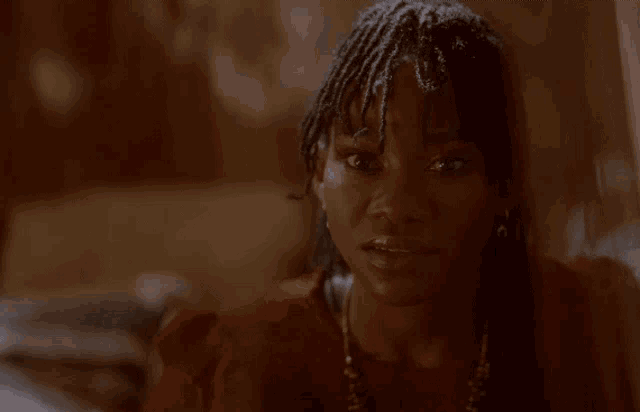 a woman with dreadlocks is wearing a red top and a necklace .