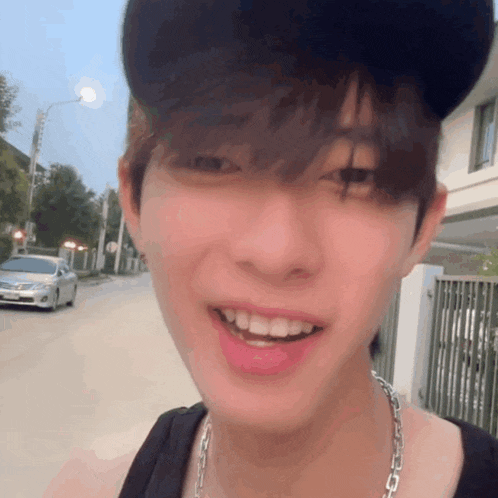 a young man wearing a hat and a necklace is smiling
