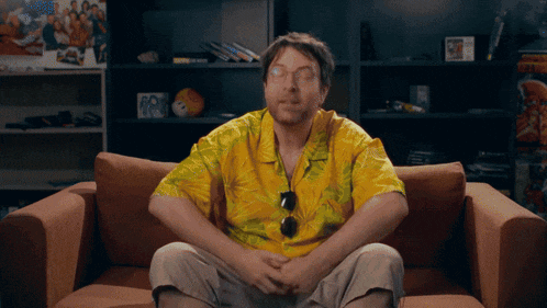 a man in a yellow shirt is sitting on a couch with his hands folded