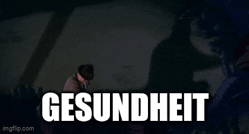 a man in a hat is holding a gun in front of a wall with the word gesundheit on it .