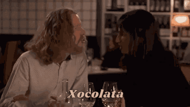 a man and a woman are sitting at a table with wine glasses and talking to each other in a restaurant .