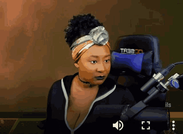 a woman wearing a headband is sitting in front of a microphone and a chair that says tr330