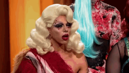 a drag queen with blonde hair and red lipstick is wearing a red dress and wig .