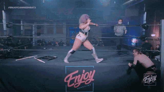 a woman with purple hair is kneeling down in a wrestling ring with the word enjoy on the bottom