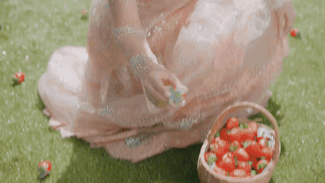 a woman in a pink dress is sitting on the grass with a flower in her hand .