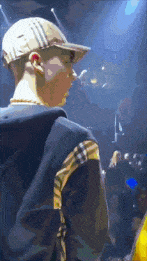 a man wearing a hat and a plaid jacket stands in front of a crowd of people