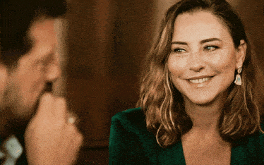 a woman in a green jacket smiles at a man in a suit