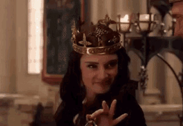 a woman wearing a crown is making a peace sign .