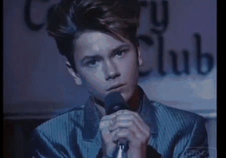 a man in a suit is singing into a microphone on a stage in front of a sign that says end ball .