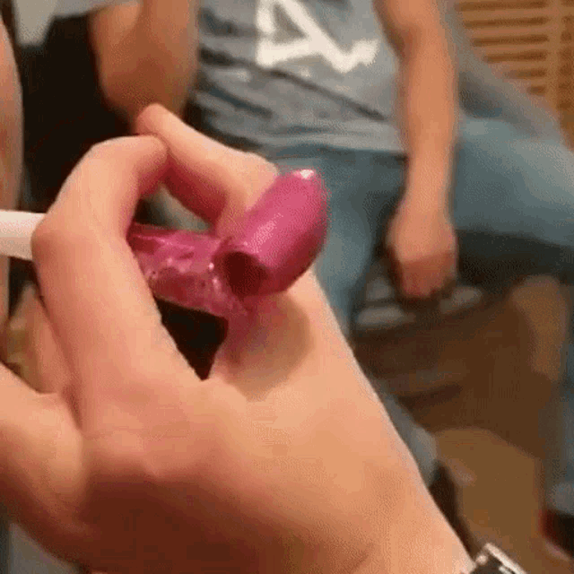 a person is holding a pink balloon in their hand and smoking a cigarette .