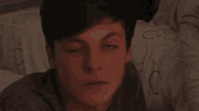 a young man with his eyes closed is laying on a bed .