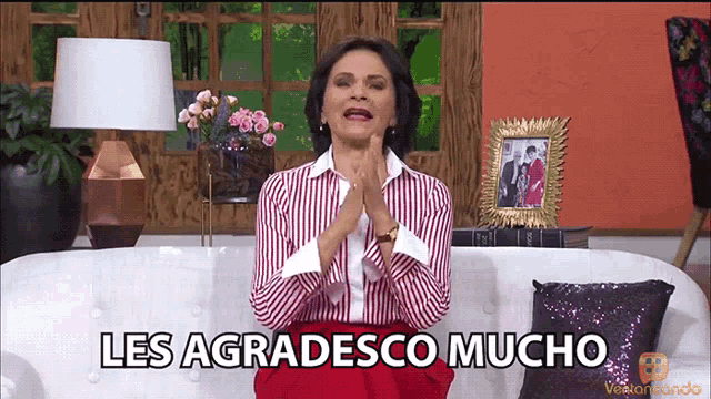 a woman in a red and white striped shirt is sitting on a couch and says les agradecisco mucho