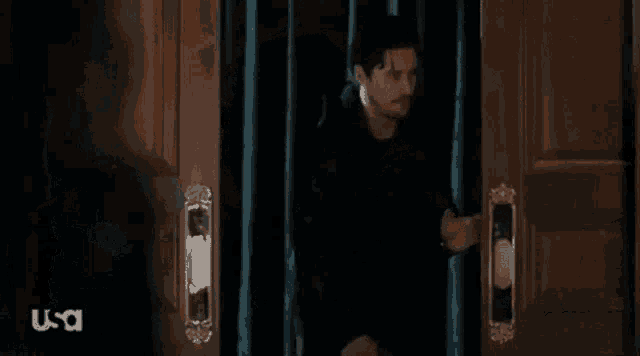 a man in a black shirt is standing in front of a door with a curtain behind him .