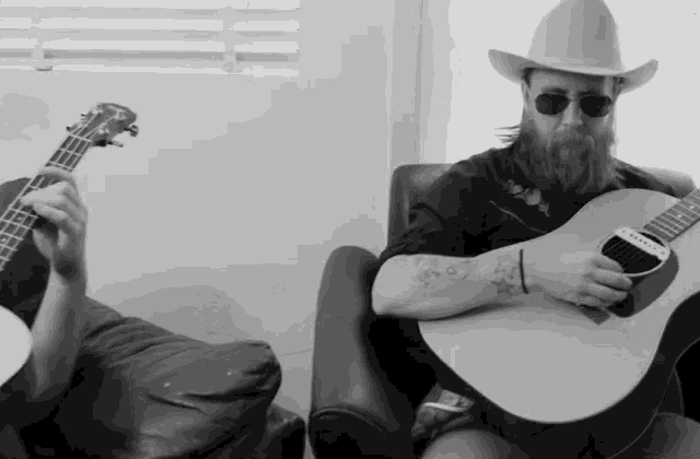 a man wearing a cowboy hat and sunglasses is holding a guitar