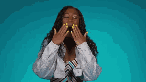 a woman with yellow nails is blowing a kiss with her hands against a blue background .