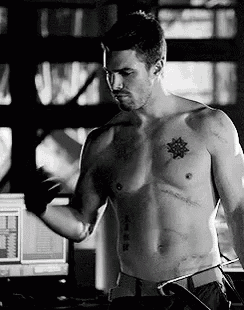 a shirtless man with a tattoo on his chest is standing in front of a computer in a black and white photo .