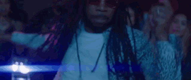 a man with dreadlocks is dancing in front of a crowd of people in a club .