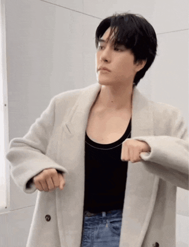 a man wearing a black tank top and a white coat is dancing .
