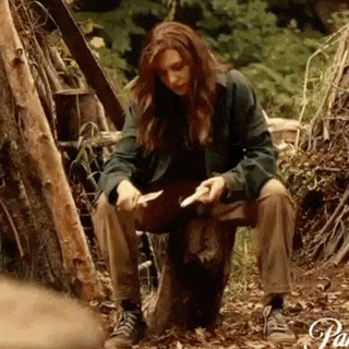 a woman is sitting on a tree stump holding a knife and a piece of paper .