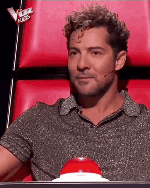 a man with curly hair is sitting in a red chair with the word kids on the back