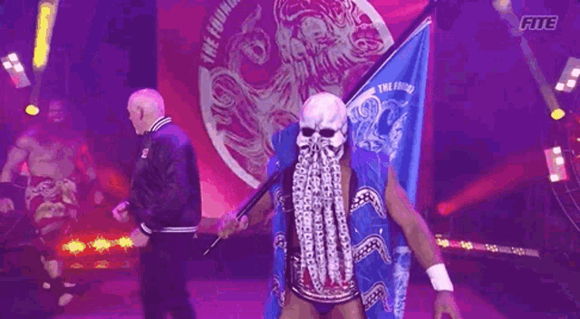 a wrestler wearing an octopus mask and holding a flag is walking down the ring .
