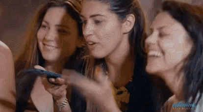 a group of three women are laughing and looking at a cell phone .
