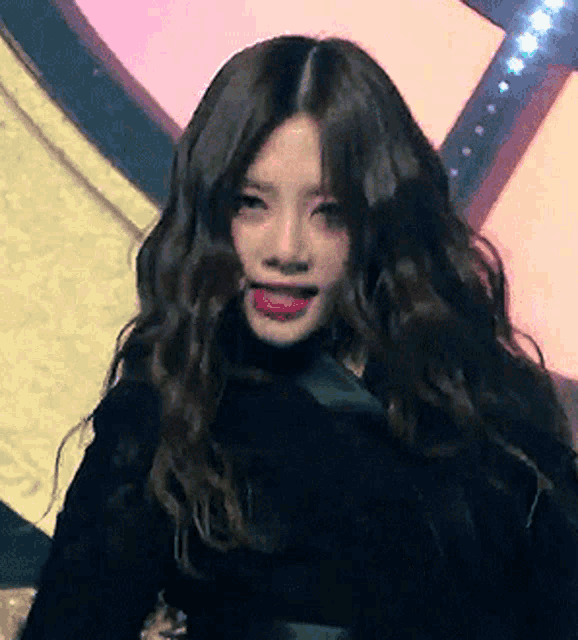 a woman with long wavy hair is wearing a black top and red lipstick