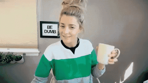 a woman is holding a cup in front of a sign that says be dumb .