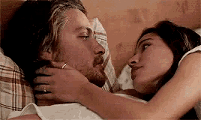 a man and a woman are laying in bed kissing .
