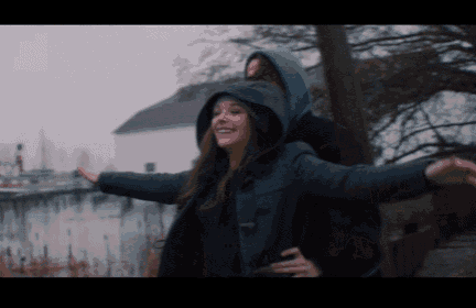 a man in a hooded jacket is carrying a woman on his back with her arms outstretched