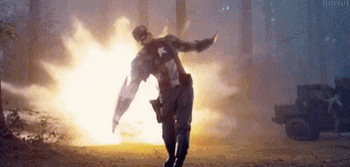 captain america is standing in front of an explosion with his shield .