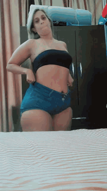 a woman in a black top and shorts is standing in front of a bed