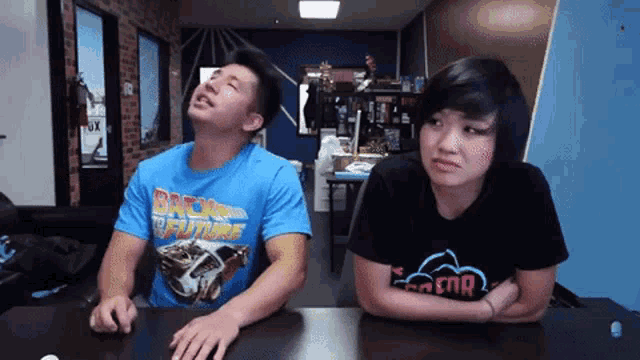 a man wearing a blue back to the future shirt sits next to a woman wearing a black shirt