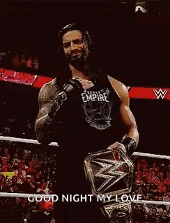 roman reigns is wearing a black tank top and holding a wrestling championship belt .