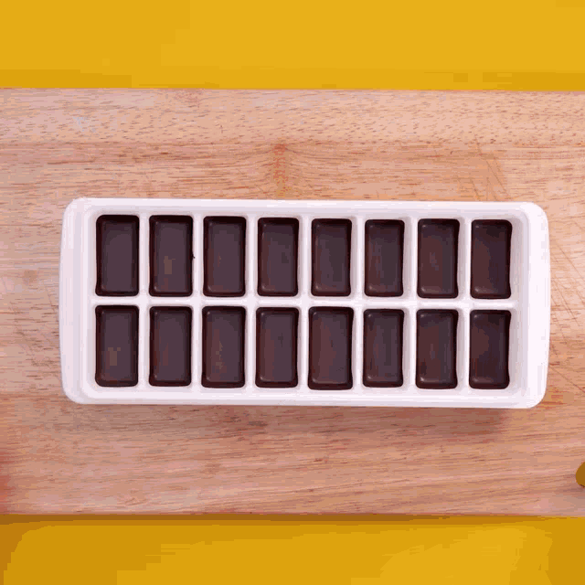 a white ice cube tray filled with chocolate squares on a wooden surface