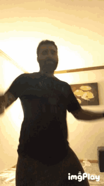 a man in a black shirt is dancing in front of a wall with a painting of flowers on it