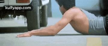a man is laying on the ground doing push ups in front of a car .