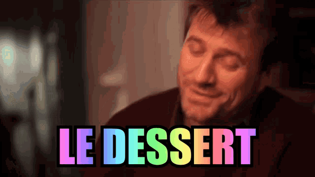 a man with his eyes closed smiles in front of a sign that reads le dessert