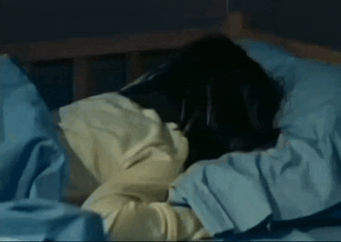 a woman is laying in bed with blue sheets and pillows .