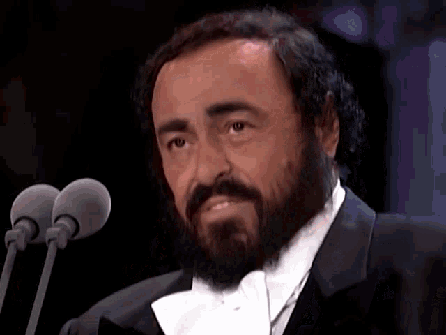 a man with a beard in a tuxedo is speaking into two microphones