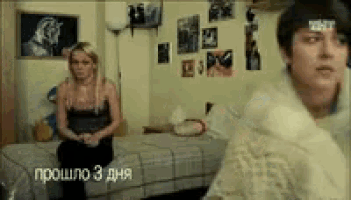 a man and a woman are sitting on a bed in a room with russian writing on the wall .