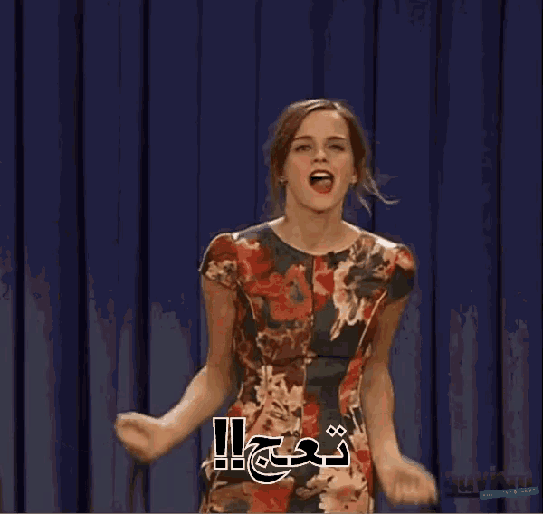 a woman in a floral dress is standing in front of a blue curtain with her hands outstretched .