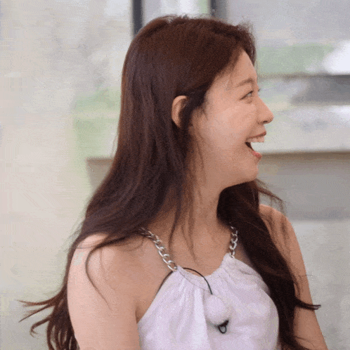 a woman wearing a white top with a chain around her neck laughs