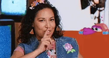 a woman in a denim vest is holding her finger to her lips