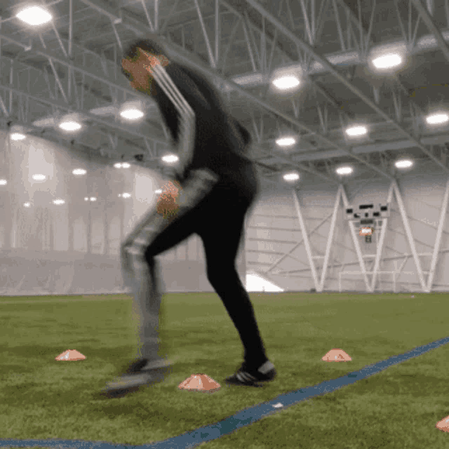 a blurred image of a person running on a field with cones in the foreground