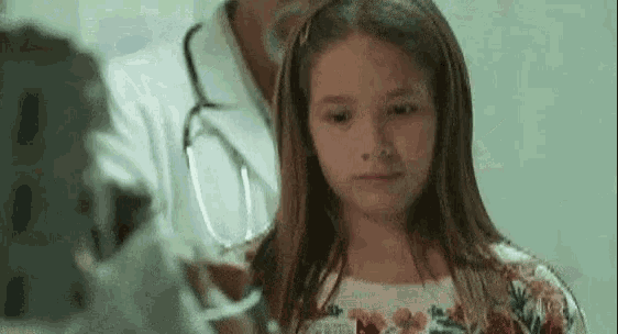 a little girl is looking at a doctor in a hospital room .