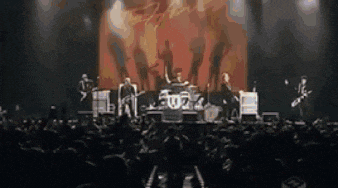 a blurry picture of a band on stage with a crowd in the background