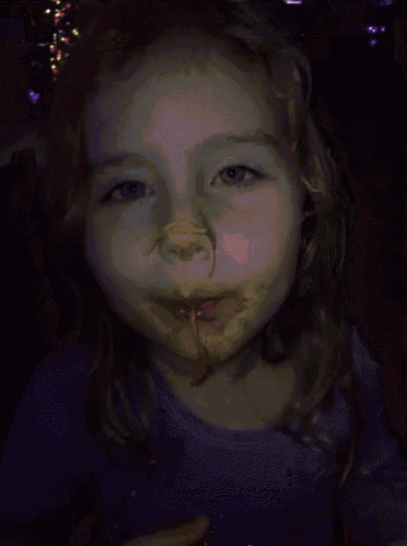 a little girl with a purple shirt on has chocolate on her face