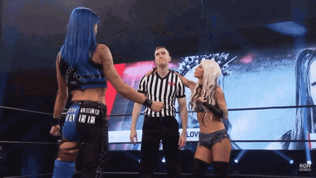 a female wrestler with blue hair talks to a referee while another wrestler looks on