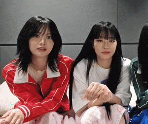 three girls are sitting next to each other and one has a red jacket on